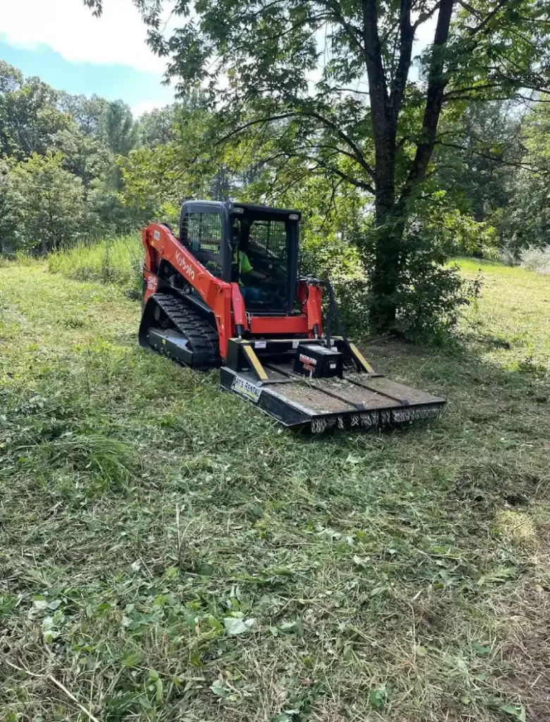 Kubota skid steer with brush cutter clearing overgrown field vegetation