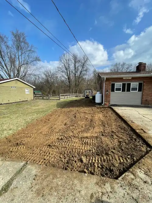 Graded area prepared for gravel driveway installation beside residential home.